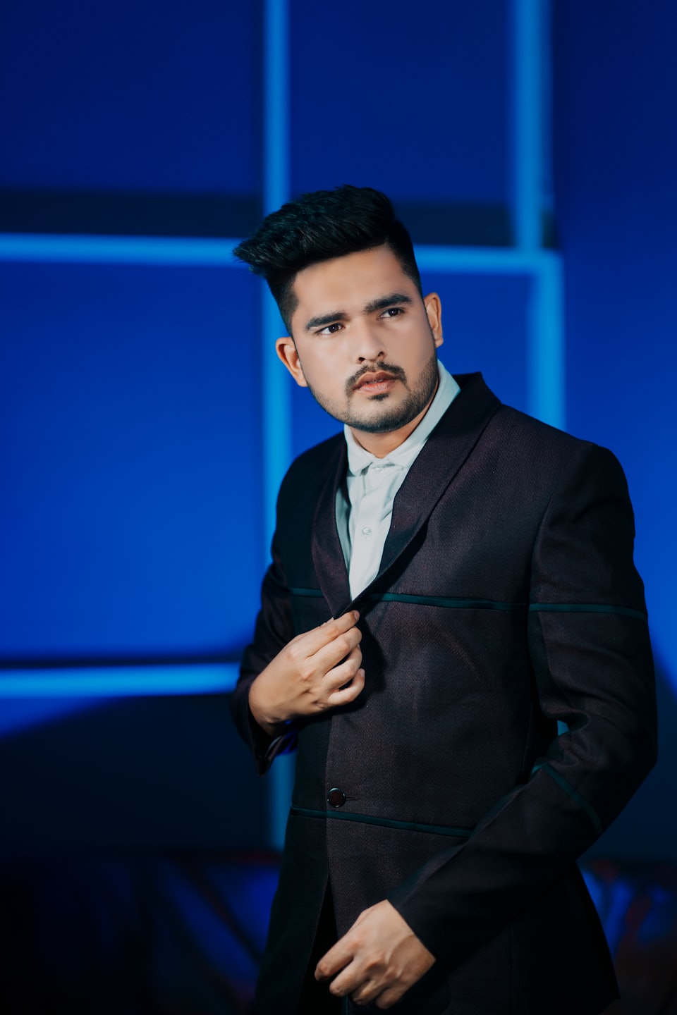 Man in a suit adjusts his lapel while posing confidently.