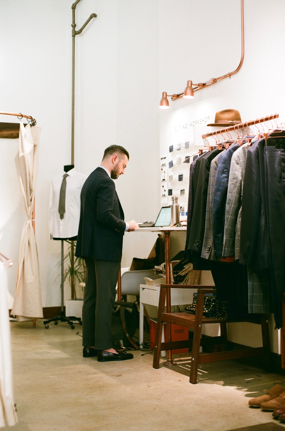 Man examines fabric swatches and laptop in a suiting workshop.