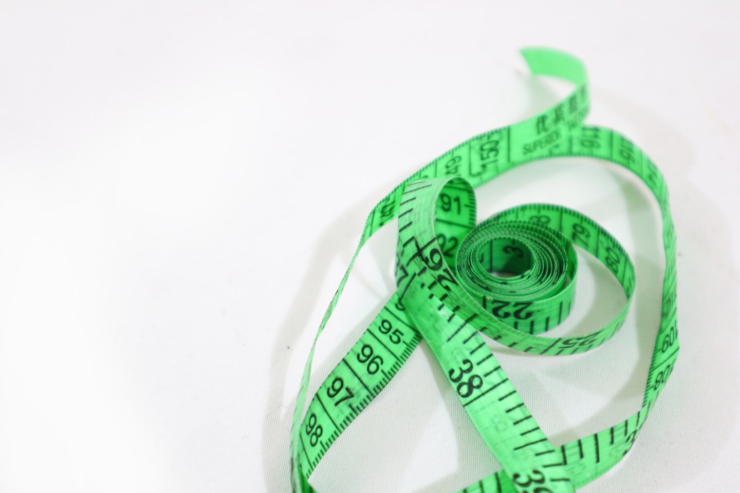 Green tailor's measuring tape unfurling on a white surface.
