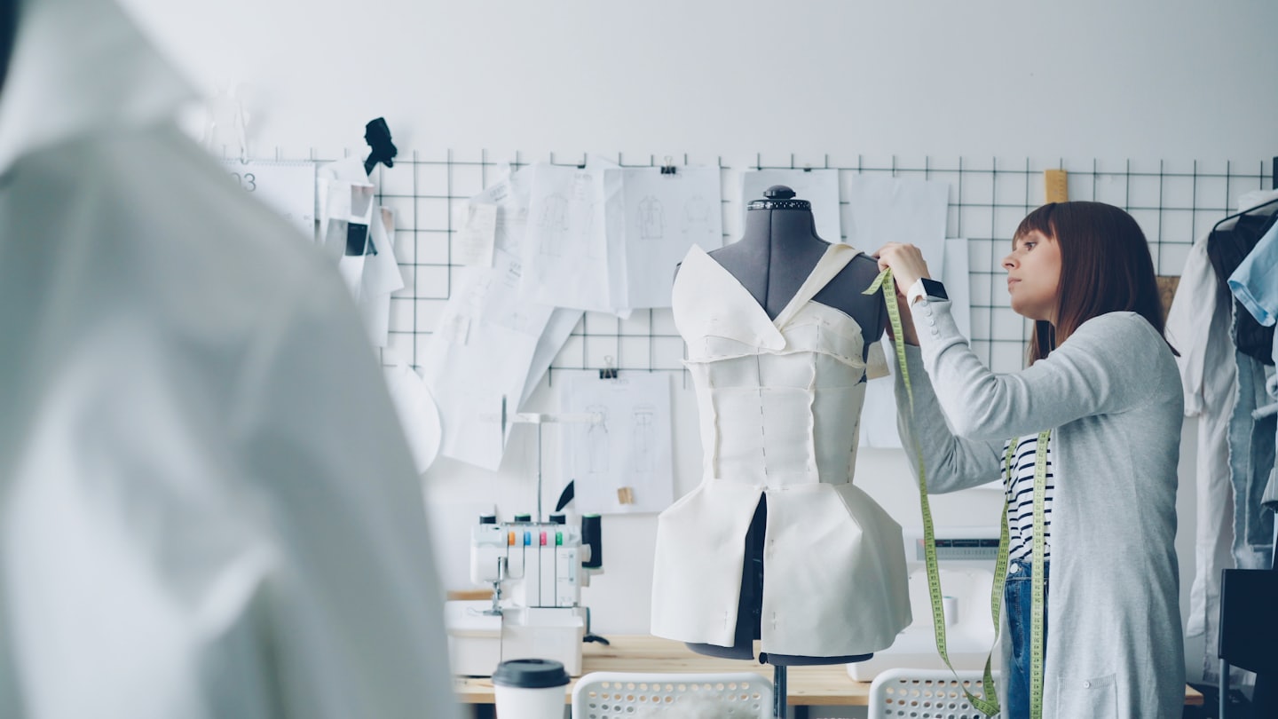 Fashion designer measures white fabric on a black dress form.