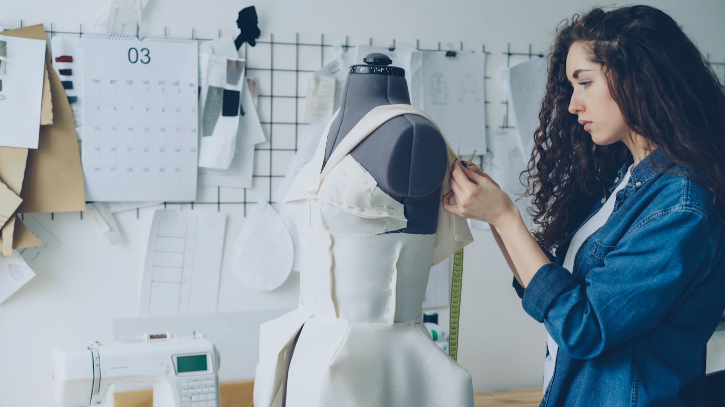 A fashion designer adjusts white fabric on a dress form.