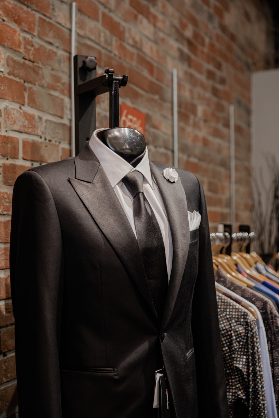 Black tuxedo suit on a mannequin in front of a brick wall.