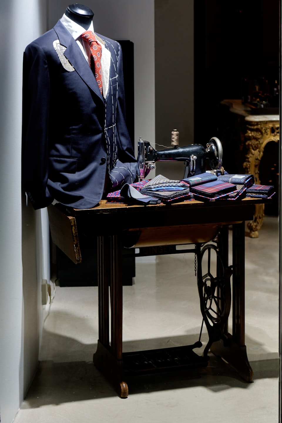 Navy suit jacket with chalk marks on a mannequin near sewing machine.